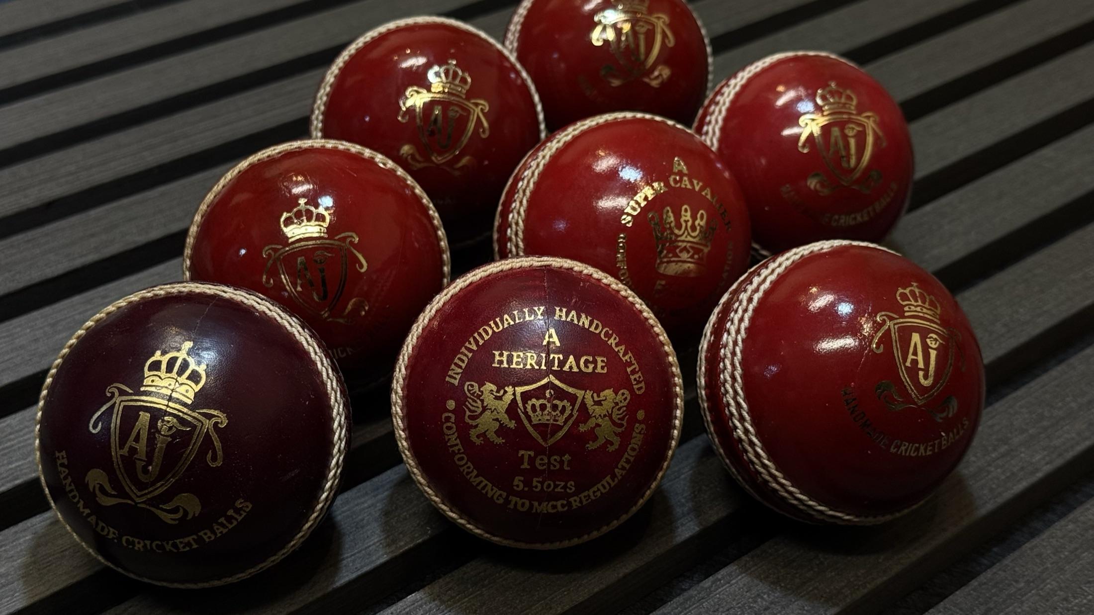 A collection of AJ cricket balls on wooden slats